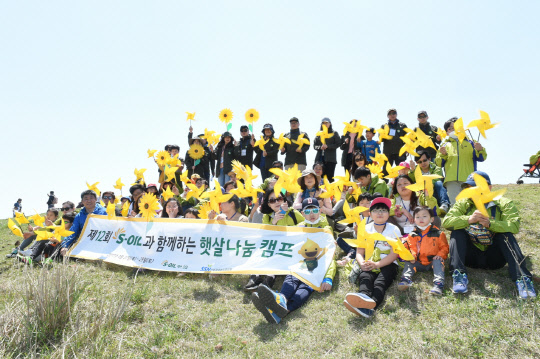 '에쓰오일 햇살나눔 캠프'에 참가한 어린이 가족과 봉사자들이 제주 용눈이 오름에 올라 소망을 적은 바람개비를 날리고 있다. 에쓰오일 제공
